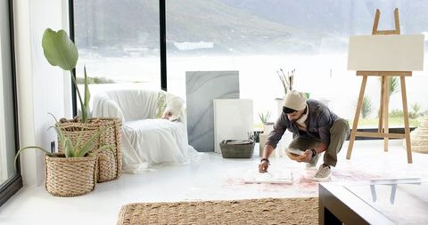 Indian male artist creating canvas on floor in sunlit coastal studio with lake view