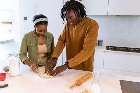 African american couple kneading dough together on bright modern kitchen counter