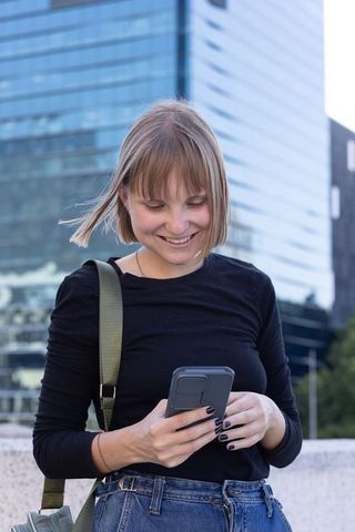 Young woman smiling and texting on smartphone amid glass highrise urban plaza
