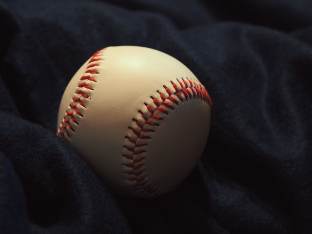 This close-up image of a baseball features detailed red stitching against a dark fabric background, highlighting the texture of the ball. Ideal for use in promotional materials for sports events, equipment advertisements, or as a background for sports-themed designs. Also effective for articles about baseball or sports in general.