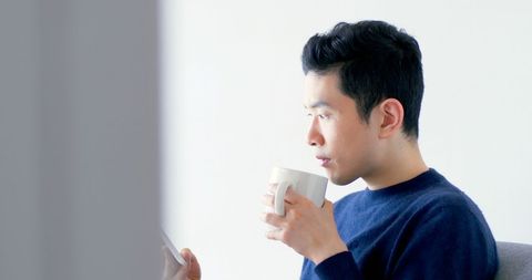 Asian Young Man Relaxing at Home Holding Coffee Cup and Tablet - Download Free Stock Images Pikwizard.com