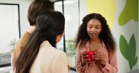 Diverse co-workers engaged in office conversation holding red mug