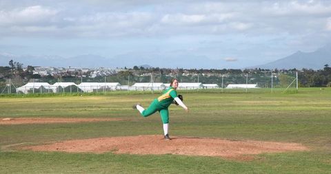 Female baseball player pitching on sunny sports field