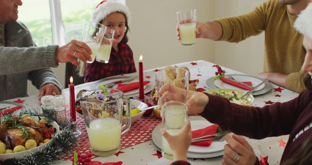 Family gathered around table celebrating Christmas with festive dinner and toasting drinks. Scene includes holiday decorations, candles and a joyful atmosphere. Suitable for holiday season promotions, greeting cards, advertisements, and family-oriented content.