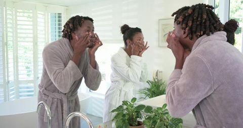 African american couple applying facial cleanser at bathroom mirror in morning routine