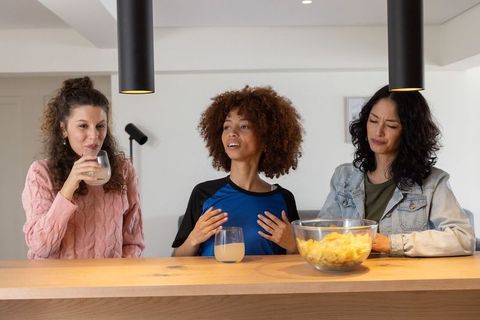 Diverse women chatting at kitchen counter with drinks and snacks casual home gathering