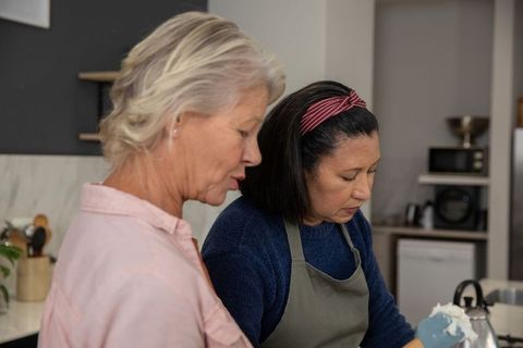 Senior friends cooking together in home kitchen mixing batter and sharing baking moment