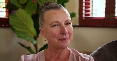 Warm smiling senior woman relaxing at home near plant