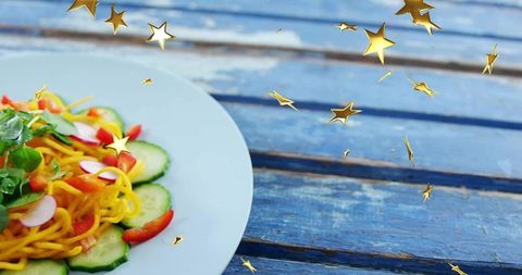Serving vibrant spiral noodle salad on weathered blue wood table with floating gold stars