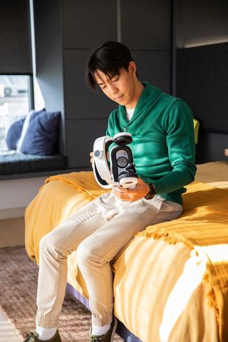 Asian man adjusting vr headset on sunlit bed in modern cozy bedroom for immersive play