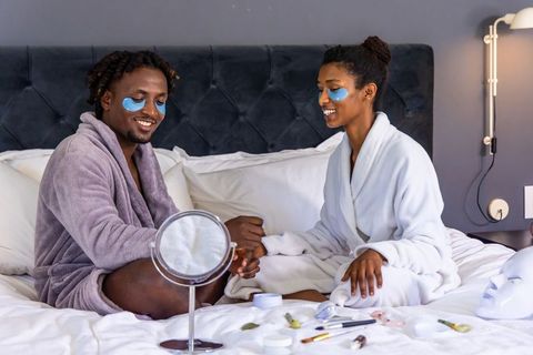 African american couple applying under-eye patches on bed enjoying cozy at-home skincare ritual