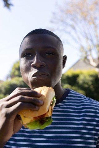 Man Enjoying Large Sandwich in Sunlit Backyard