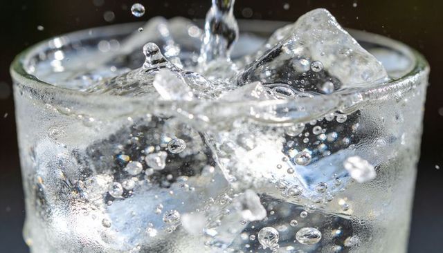 Pouring sparkling water with ice, bubbling splash and condensation on glass macro closeup