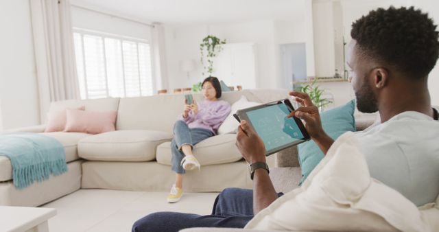 Diverse couple sitting on couch and using tablet in living room - Download Free Stock Photos Pikwizard.com
