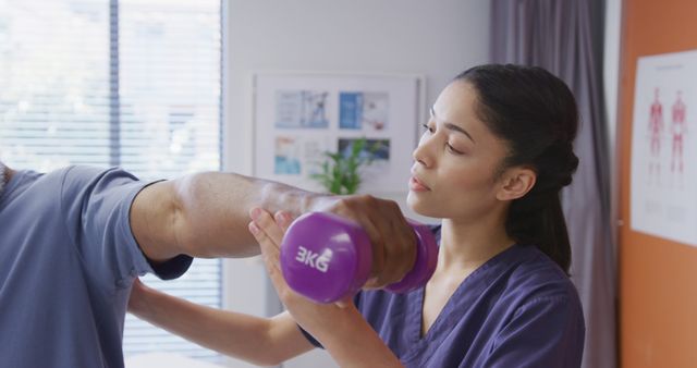 Diverse female physiotherapist and senior male patient holding dumbbell at physical therapy session. Medicine, healthcare, lifestyle and hospital concept.