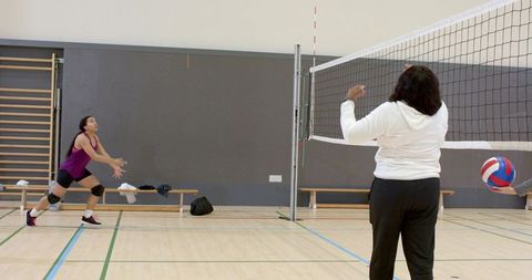 Diverse women practicing volleyball indoors showing teamwork, net play and athletic training