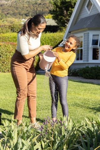 Mother and daughter watering plants in sunlit backyard garden, family gardening activity