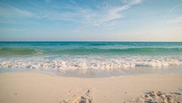 Turquoise waves rolling onto pristine white sand beach under sunny tranquil sky