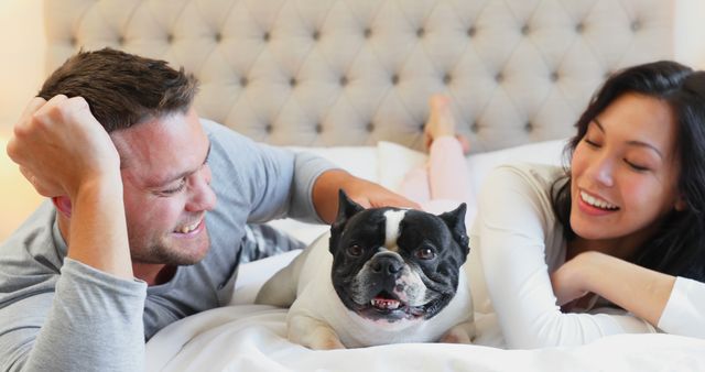 A cheerful couple lying on a comfortable bed with their French Bulldog, creating a warm and joyful atmosphere. Perfect for use in advertising campaigns about pet products, home living, family happiness, or lifestyle blogs and articles about pet ownership and family bonding.