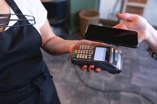 Hairdresser holding payment terminal while customer makes contactless payment with smartphone. Ideal for illustrating modern payment methods, hygiene practices in service industries, and COVID-19 safety measures.