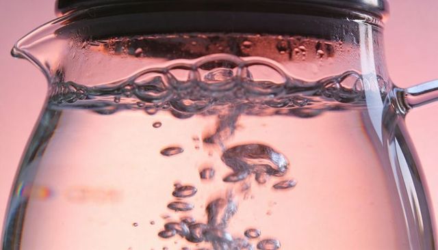 Macro glass kettle boiling with rising bubble stream on pink studio background