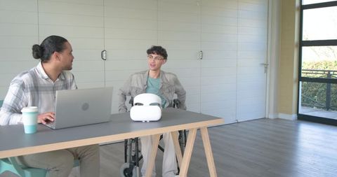 Collaborating team discussing project with wheelchair user and vr headset on workspace