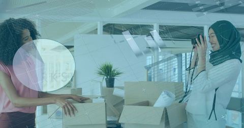 Young coworkers unpacking office boxes while photographer in hijab documenting relocation