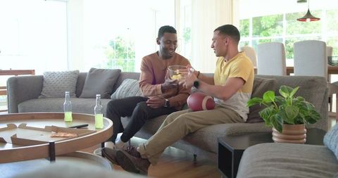 Diverse Friends Sharing Snacks and Cheering While Watching Football on Modern Living Couch