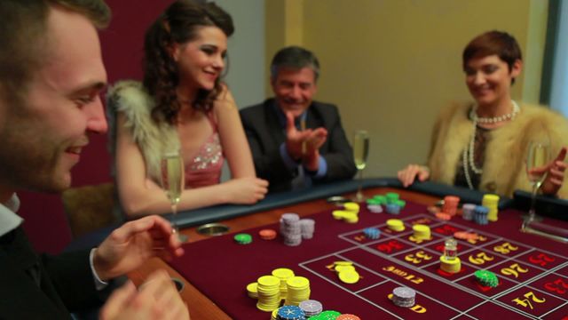 Group of elegantly dressed friends celebrating a win at a casino roulette table. People clapping, smiling, and toasting with glasses of champagne. Roulette chips prominently displayed on the table. Ideal for topics related to gambling, luxury lifestyle, success, celebration, and social gatherings.