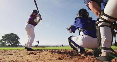 Low-Angle Youth Female Batter Swinging at Baseball Diamond with Catcher Crouching