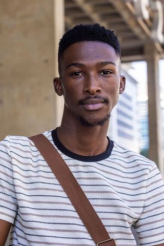 African man standing under metal beams wearing striped knit shirt and crossbody strap