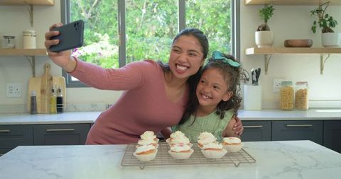 Mother and daughter taking selfie with homemade cupcakes in bright modern kitchen