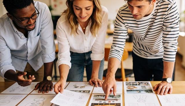 Creative team reviewing design sketches and mockups on wooden table collaborating on branding