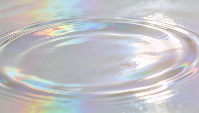 Iridescent liquid ripples creating concentric rings on pastel water surface