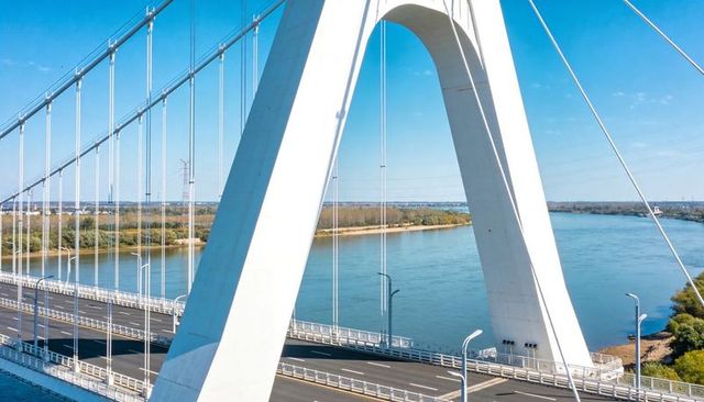 A-shaped White Suspension Bridge Arch Framing Blue River Span over Empty Highway with Minimalist Mod