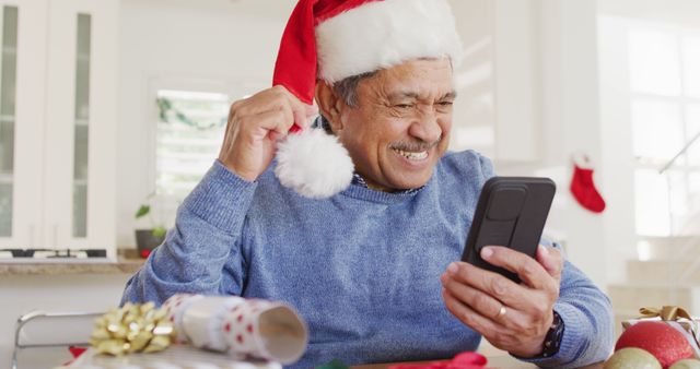 Senior man wearing Santa hat smiling while using smartphone, adds a touch of joy and festivity. Perfect for holiday marketing, technology use among elderly, or Christmas greeting cards.