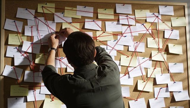 Investigator pinning index cards on cork board linking clues with red string case connection map