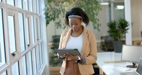 African american woman using tablet in bright open office, wearing smartwatch and blazer