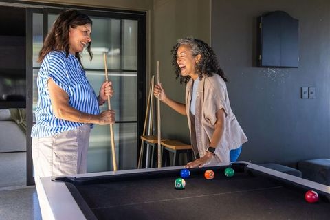Diverse women laughing and playing pool in modern cozy home game room for casual social fun