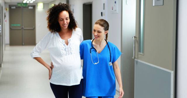 Pregnant woman accompanied by nurse walking in a hospital hallway. Nurse wearing blue scrubs and stethoscope, offering support and care. Useful for themes related to pregnancy, maternity, healthcare, prenatal care, and patient support in medical facilities.