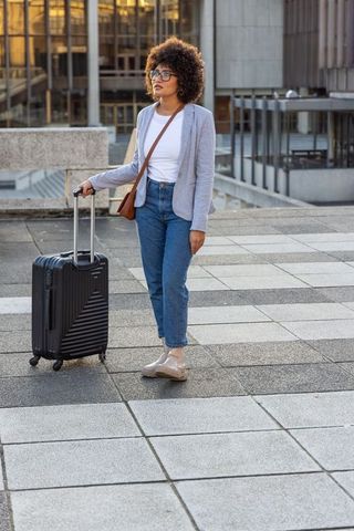 African american woman standing with suitcase on urban plaza during golden hour