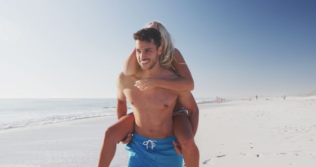 Happy diverse couple smiling and playing piggy back on beach. Lifestyle, realxation, nature, free time and vacation.