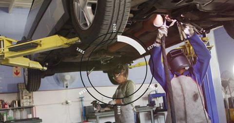 Mechanics repairing car undercarriage on hydraulic lift with welding helmet and tools