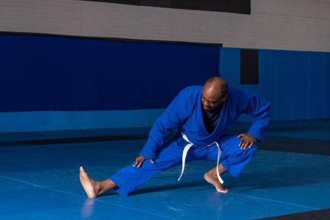 Martial artist wearing blue gi performing stretch on training mats