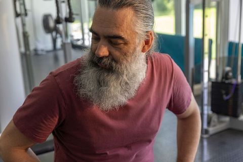Bearded mature man resting on weight bench reflecting after workout in modern gym