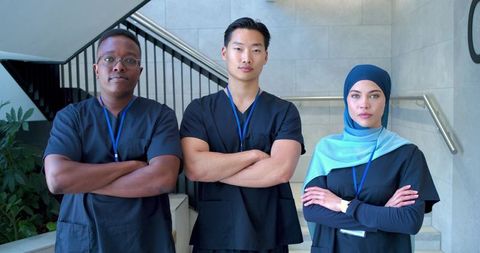 Multicultural medical team standing with arms crossed in clinical stairwell for teamwork