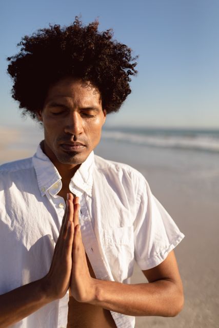 Young African-American man practicing yoga and meditation on a serene beach. Ideal for use in wellness, mindfulness, and mental health content, promoting relaxation, self-care, and spiritual practices. Perfect for articles, blogs, and advertisements focused on healthy living and outdoor activities.