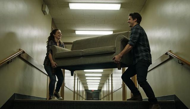 Young couple carrying sofa up narrow stairwell, teamwork during move in apartment hallway