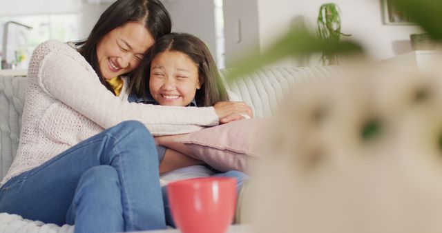 Image of happy asian mother and daughter sitting on sofa and having fun. Family, motherhood, relations and spending quality time together concept digitally generated image.