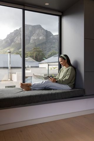 Asian woman using tablet on cozy window seat with mountain view in minimalist home office
